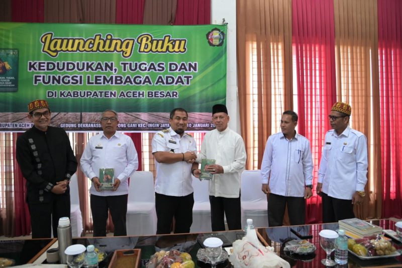 Pj Bupati Aceh Besar didampingi Asisten 1 Farhan AP menyerahkan buku secara simbolis kepada salah satu peserta launching buku Kedudukan, Tugas dan Fungsi Lembaga Adat Aceh Besar di Gedung Dekranasda, Gampong Gani, Kecamatan Ingin Jaya, Rabu (10/01/2024).