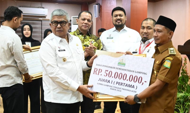 Pj Gubernur Aceh Bustami Hamzah SE MSi bersama Pj Bupati Aceh Besar Muhammad Iswanto, S.STP MM menyerahkan Dana Pembinaan juara 1 lomba gampong tingkat Provinsi Aceh tahun 2024 Kepada Keuchik Bueng Sidom, Kecamatan Blang Bintang Aceh Besar di Gedung Serbaguna Setda Aceh, Banda Aceh, Jumat (05/97/2024). Foto: MC Aceh Besar. 